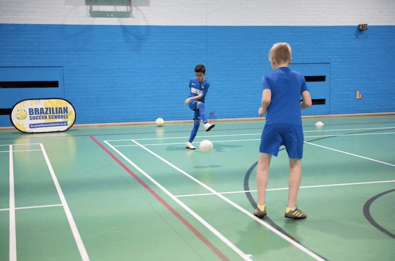Futebol de Salão. Image shows a Brazilian Soccer Schools class where two boys are kicking the ball to eachother working on their skills.