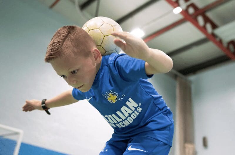 Benefits of football training for 9 year olds. Image shows a boy balancing a football on top of his neck in a BSS training session.