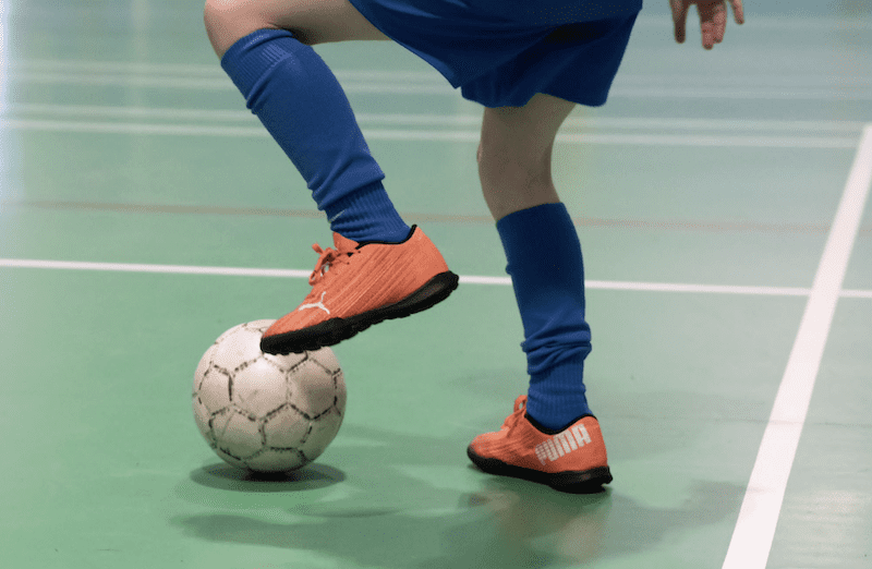 Football clubs for kids near me. Image shows a kid with orange football boots touching the football with their foot. 
