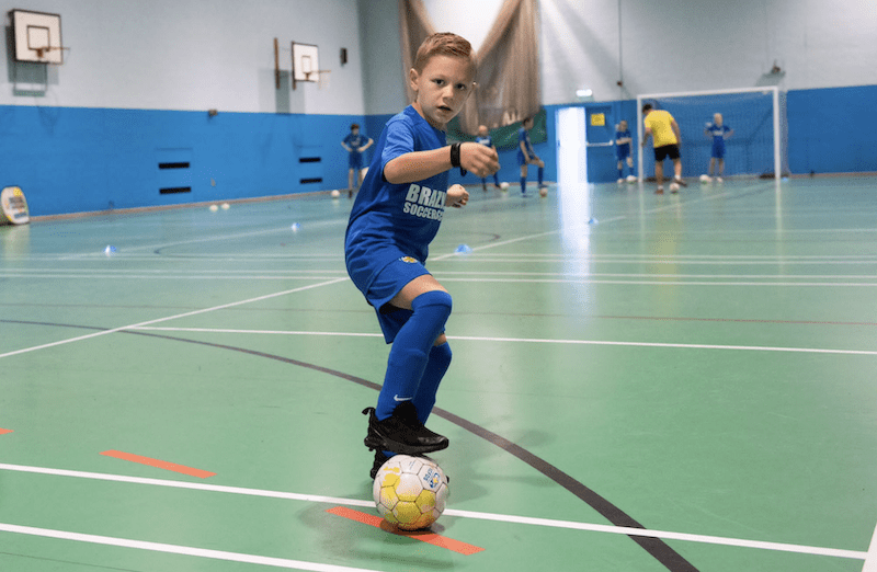 Kids football training in Bedford. Image shows a boy during a Brazilian Soccer Schools football class with his foot on top of a BSS football. 