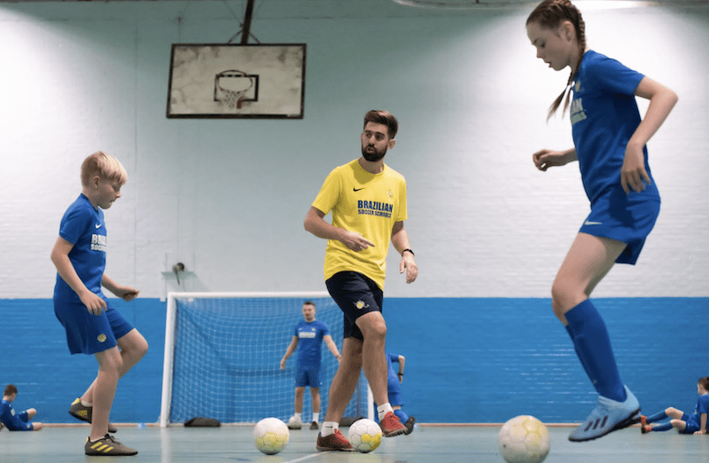 Kids football training Milton Keynes. Image shows a brazilian soccer schools coach teaching a girl and a boy during a kids football session.
